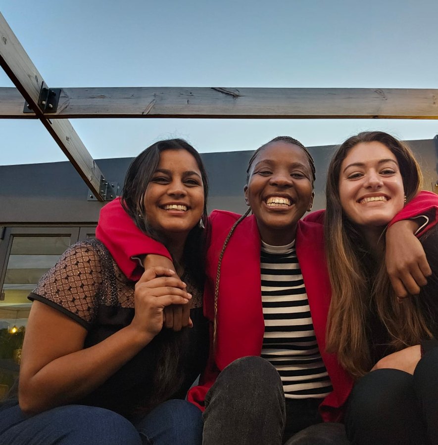 Three friends smiling together on a rooftop at sunset